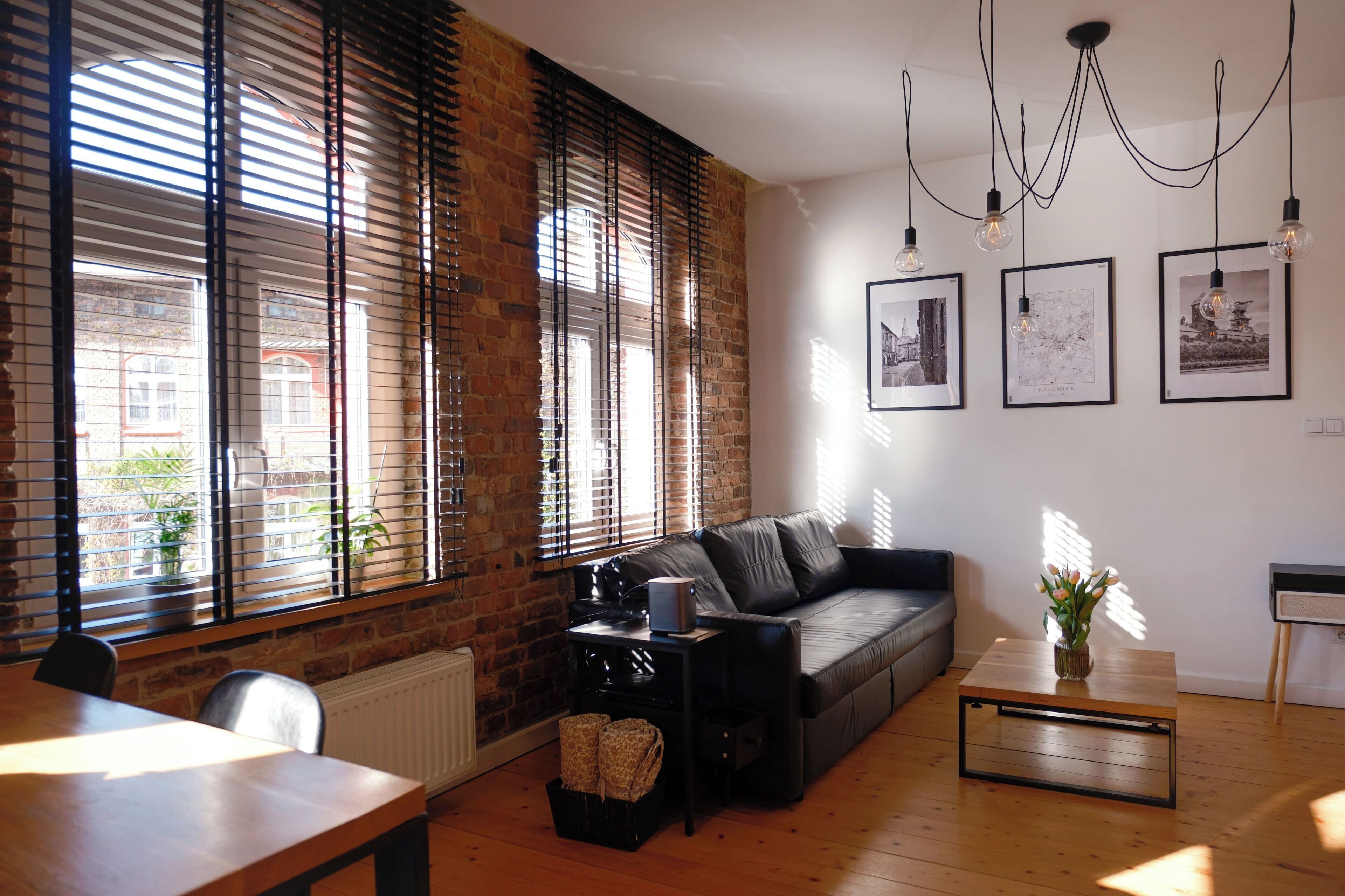 A living room with a sofa, a coffee table, a dining table, and a fireplace. There are three framed pictures on the wall.