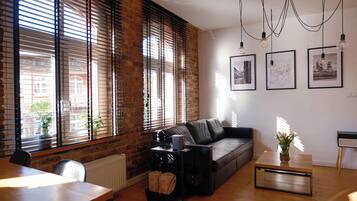A living room with a sofa, a coffee table, a dining table, and a fireplace. There are three framed pictures on the wall.