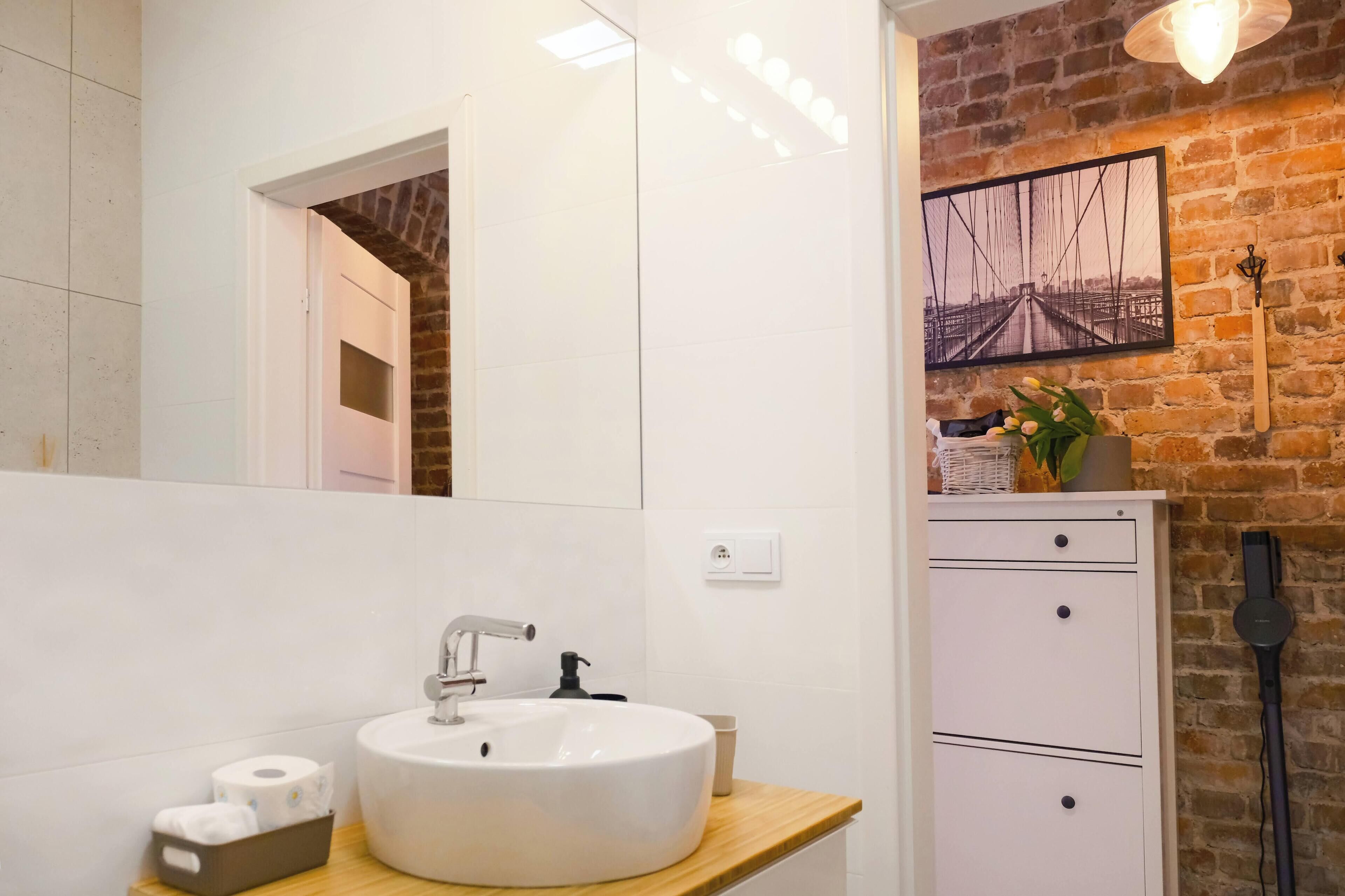 A bathroom with a white sink, mirror, and a brick wall.