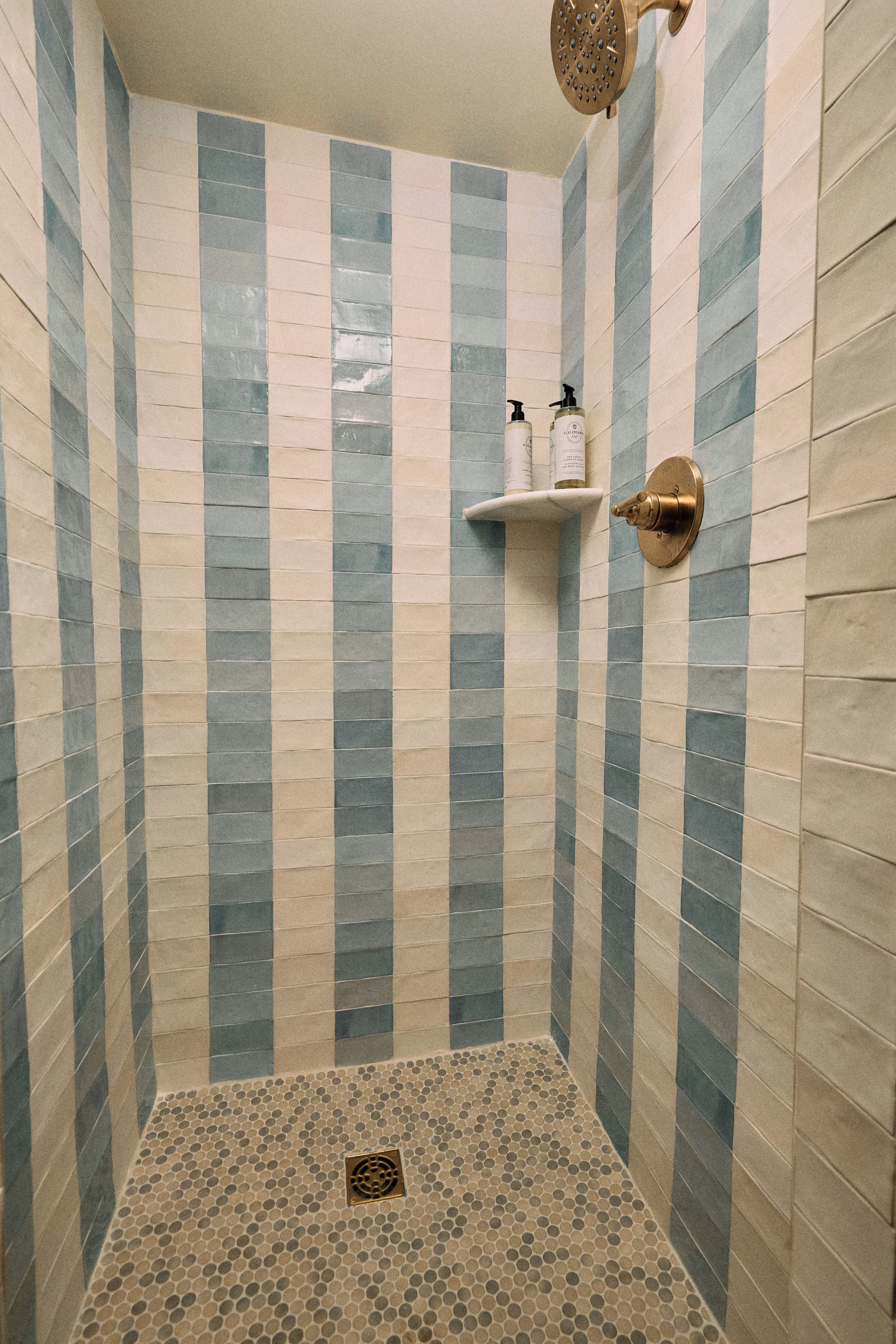 A shower with a tiled wall featuring a striped pattern and a showerhead mounted on the wall.