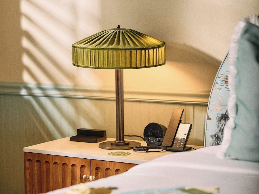 A hotel room with a bed, a bedside table with a lamp, a telephone, and a clock.