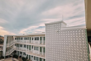 Um edifício com vários andares, fachada branca e uma lateral com padrão, além de uma escadaria que dá acesso a um andar superior.