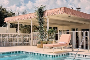 A pool area with a covered seating area, lounge chairs, and a fence. - Hotel Margot (Pensacola)
