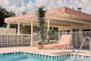 A pool area with a covered seating area, lounge chairs, and a fence.