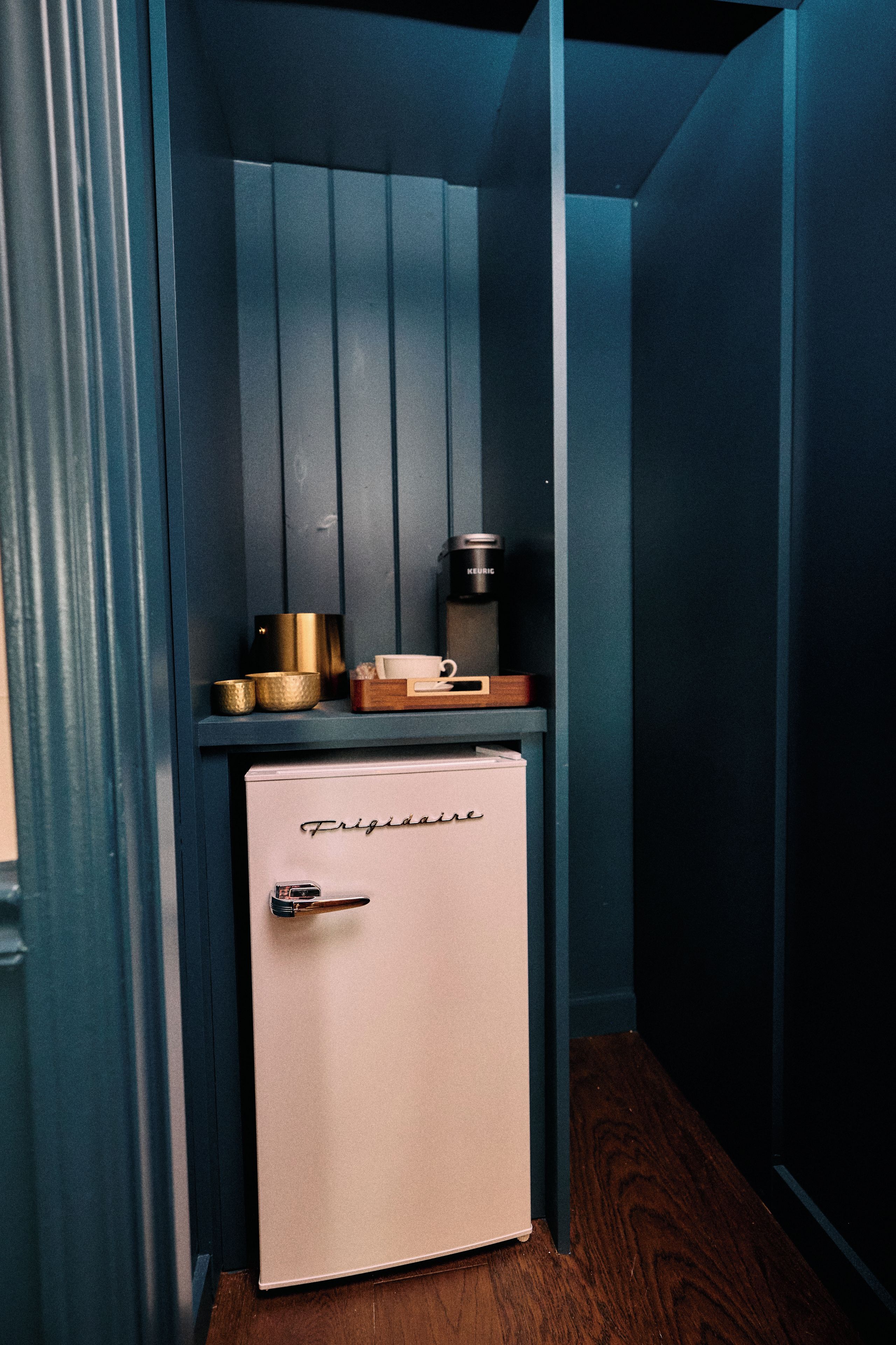 A compact kitchenette with a white refrigerator, a coffee maker, and a small wooden box on top.