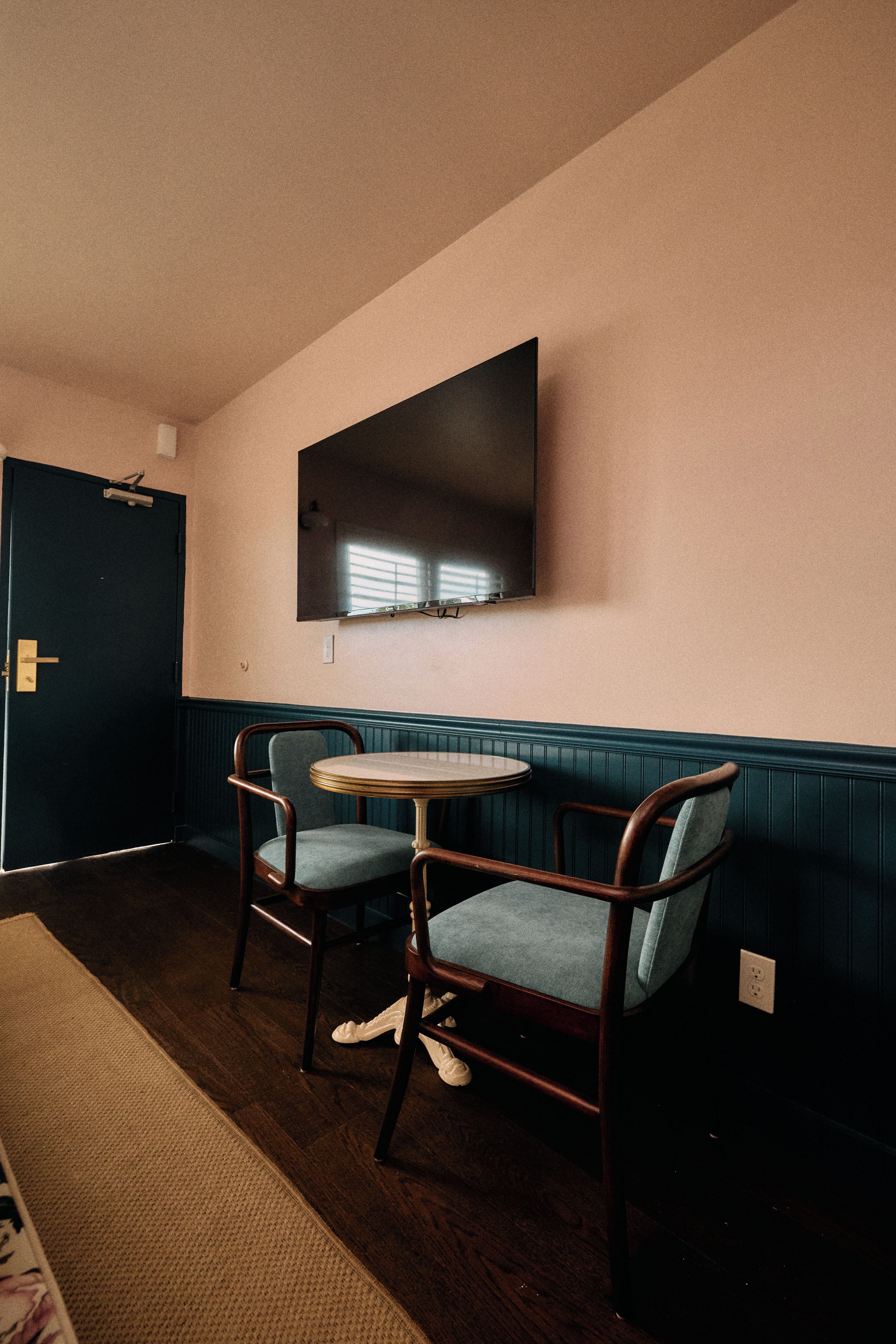 A room with a dark door, a wall-mounted flat-screen TV, a round table, and two chairs.