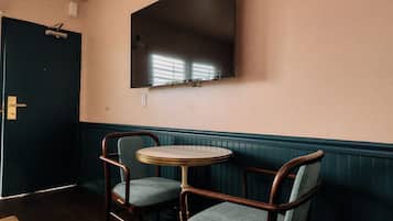 A room with a dark door, a wall-mounted flat-screen TV, a round table, and two chairs.