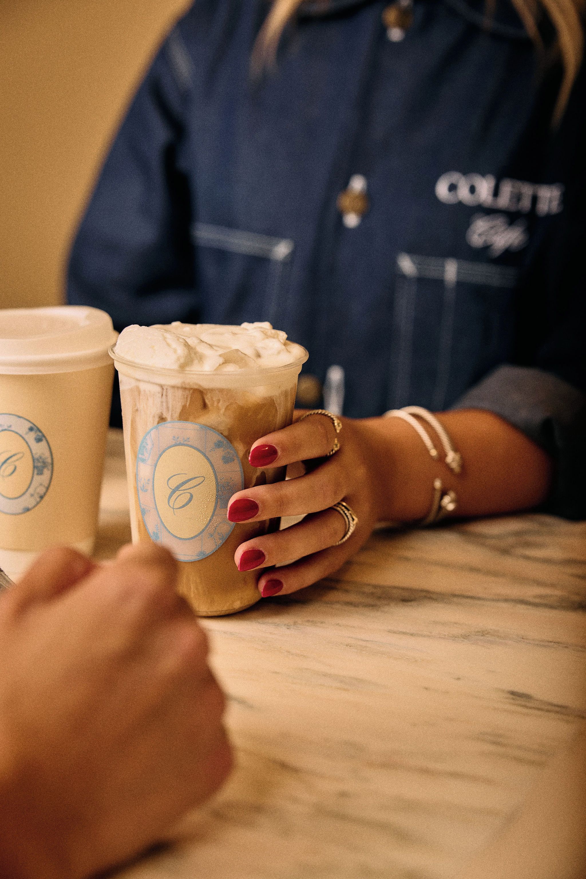 A person holding a cup with a logo, seated at a table with another cup beside them.