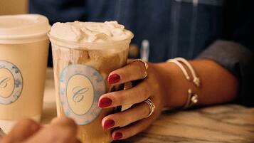 A person holding a cup with a logo, seated at a table with another cup beside them.