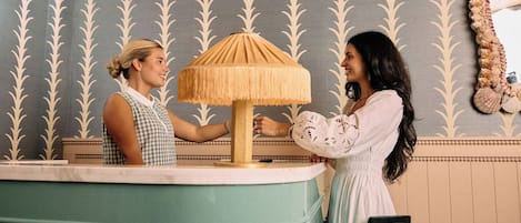 Aula, jossa on vastaanottotiski, lamppu ja seinällä peili.