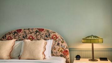 Una cama con cabecera de flores, una lámpara de noche y un reloj sobre la mesita.