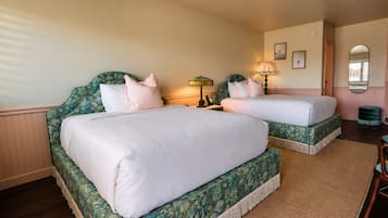 A hotel room with two beds, a nightstand, a lamp, a mirror, and a small table.