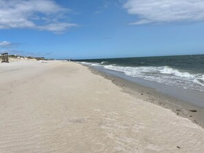Ein weiter Sandstrand mit sanften Wellen, einem klaren Himmel und einem Rettungsturm links.