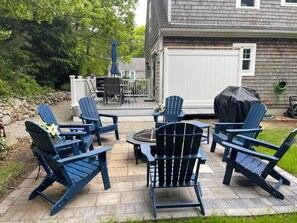 Eine Terrasse mit Adirondack-Stühlen, einem Tisch und einem Grill.