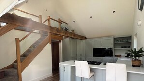 Eine Küche mit einer Holztreppe, grauen Schränken, einer weißen Arbeitsplatte und einer kleinen Kücheninsel mit Barhocker.