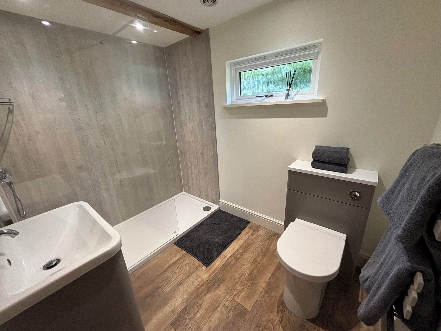 Un baño con ducha, lavabo, inodoro, una ventana y un estante pequeño.