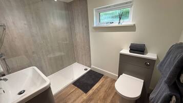 Un baño con ducha, lavabo, inodoro, una ventana y un estante pequeño.