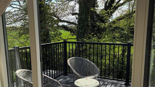 Ein Balkon mit Korbstühlen und einem gemusterten Teppich, umgeben von einem schwarzen Geländer und einem Baum.
