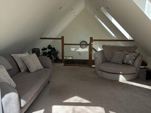 Ein Loft-Zimmer mit schrägem Dach, zwei Sofas, einem Holzrahmenfenster und einem Blumentopf.