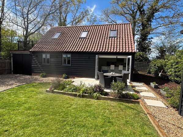 A house with a tiled roof, a patio with chairs, and a garden with plants and a lawn. - Ash Tree Lodge (Norwich)