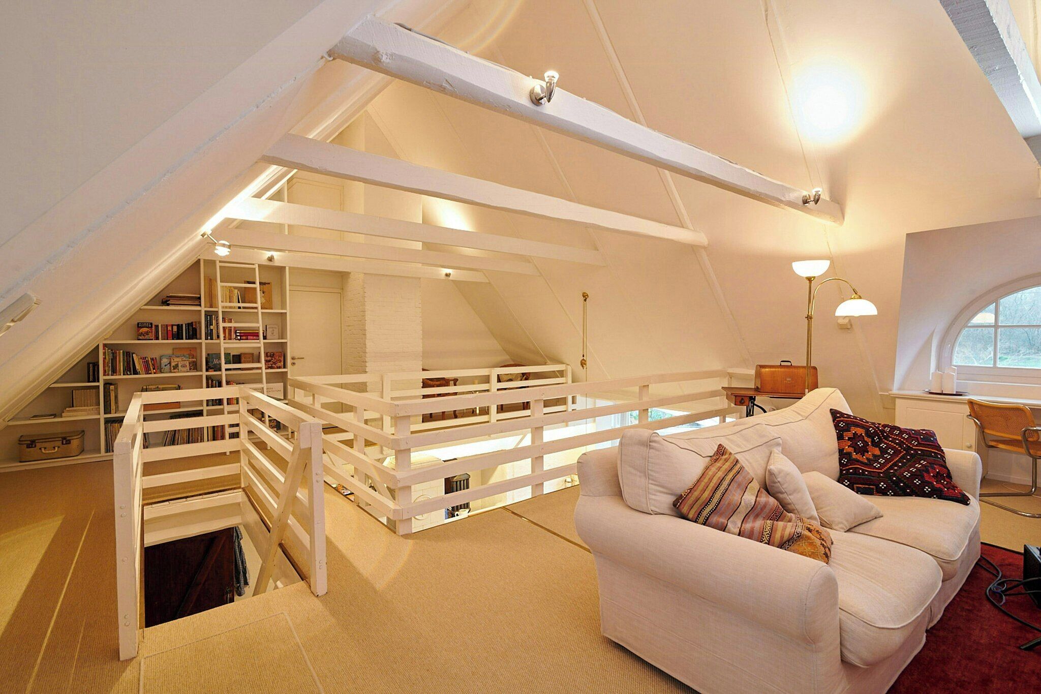 A loft bedroom with a white bed, a white sofa, a desk, and a bookshelf. - Charming country house in Schleswig-Holstein (Fedderingen)