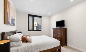 A bedroom with a bed, a dresser, a television, and a window with blinds.