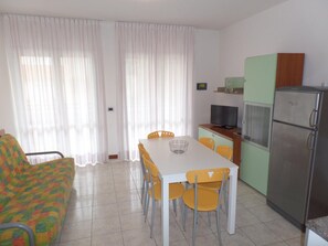 Ein kompakter Wohnbereich mit Esstisch, Stühlen, einer Couch, einem Fernseher und einem Kühlschrank.