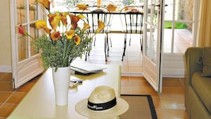 Una habitación con una mesa de comedor, sillas, un florero con flores, un sombrero y una ventana con vistas a follaje.