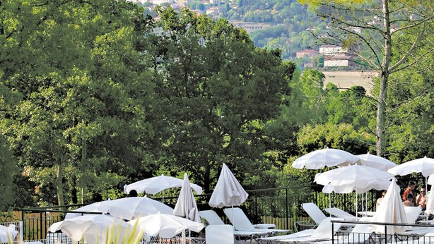 Une terrasse dotée de chaises longues et de parasols, offrant une vue sur un village perché sur une colline.