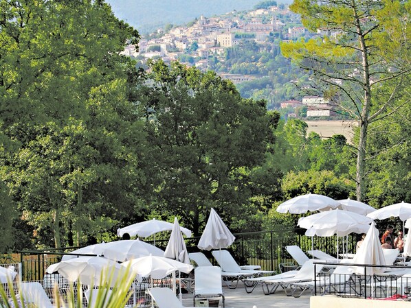 Una terraza con tumbonas y sombrillas, con vistas a un pueblo en la ladera de una colina.