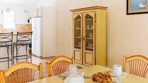 Comedor con una mesa dispuesta para cuatro, sillas, un aparador con puertas de cristal y una cocina al fondo.