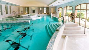 Une piscine intérieure à l’eau claire, avec des marches permettant d’y accéder, et une vue sur la verdure environnante.