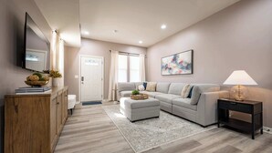 A modern living room with a grey sofa, a wooden cabinet, a small side table with a lamp, and a large abstract painting on the wall. - Luxurious, Modern Duplex | 6 Bedrooms! Sleeps 12+ (Indianapolis)