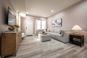 A modern living room with a grey sofa, a wooden cabinet, a black nightstand, and a floor lamp. - Luxurious, Modern Duplex | 6 Bedrooms! Sleeps 12+ (Indianapolis)