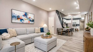A modern living room with a sectional sofa, a coffee table, and a dining area with a table and chairs. - Luxurious, Modern Duplex | 6 Bedrooms! Sleeps 12+ (Indianapolis)