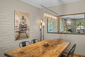 Ein Essbereich mit einem Holztisch, Stühlen, einem großen Spiegel, einer Lüster und einem Wandbild mit einem Oldtimer-Zug.