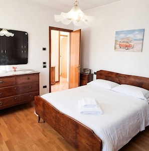 Um quarto com cama de madeira, cômoda, penteadeira com espelho, rádio e pintura com tema praiano.