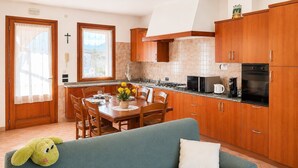 Una cucina con mobili in legno, un tavolo da pranzo con sedie, un divano e una finestra con tende.