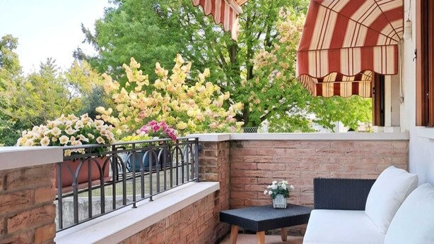 Un patio con un muro in mattoni, un divano in rattan nero, un tavolino e un tendaggio a righe.