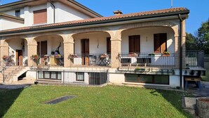 Una casa a due piani con patio coperto, posti a sedere all'aperto e un piccolo giardino.