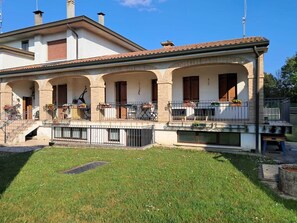 Una casa de dos pisos con un porche cubierto, mobiliario exterior y un pequeño jardín.