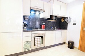 A kitchen with white cabinets, a black countertop, a stove, a microwave, and a trash bin. - Dar Yanis -(2-4 Guests) -Beach on foot - A/C - Terrace - Parking - 2 Netflix TVs (Imi Ouaddar)