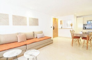 Uma sala de estar moderna com um sofá, duas mesas laterais e uma área de jantar com uma mesa e cadeiras de madeira.