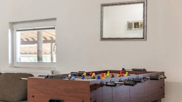 A room with a wooden foosball table, a sofa, and a window with blinds.