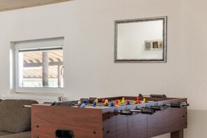 Una habitación con mesa de futbolín de madera, un sofá y una ventana con persianas.