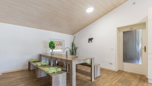 Una habitación con techo de madera, una mesa de comedor con bancos, una planta en maceta y una puerta con un cartel de 'No Fumar'.