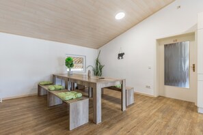 A room with a wooden ceiling, a dining table with benches, a potted plant, and a door with a 'No Smoking' sign.