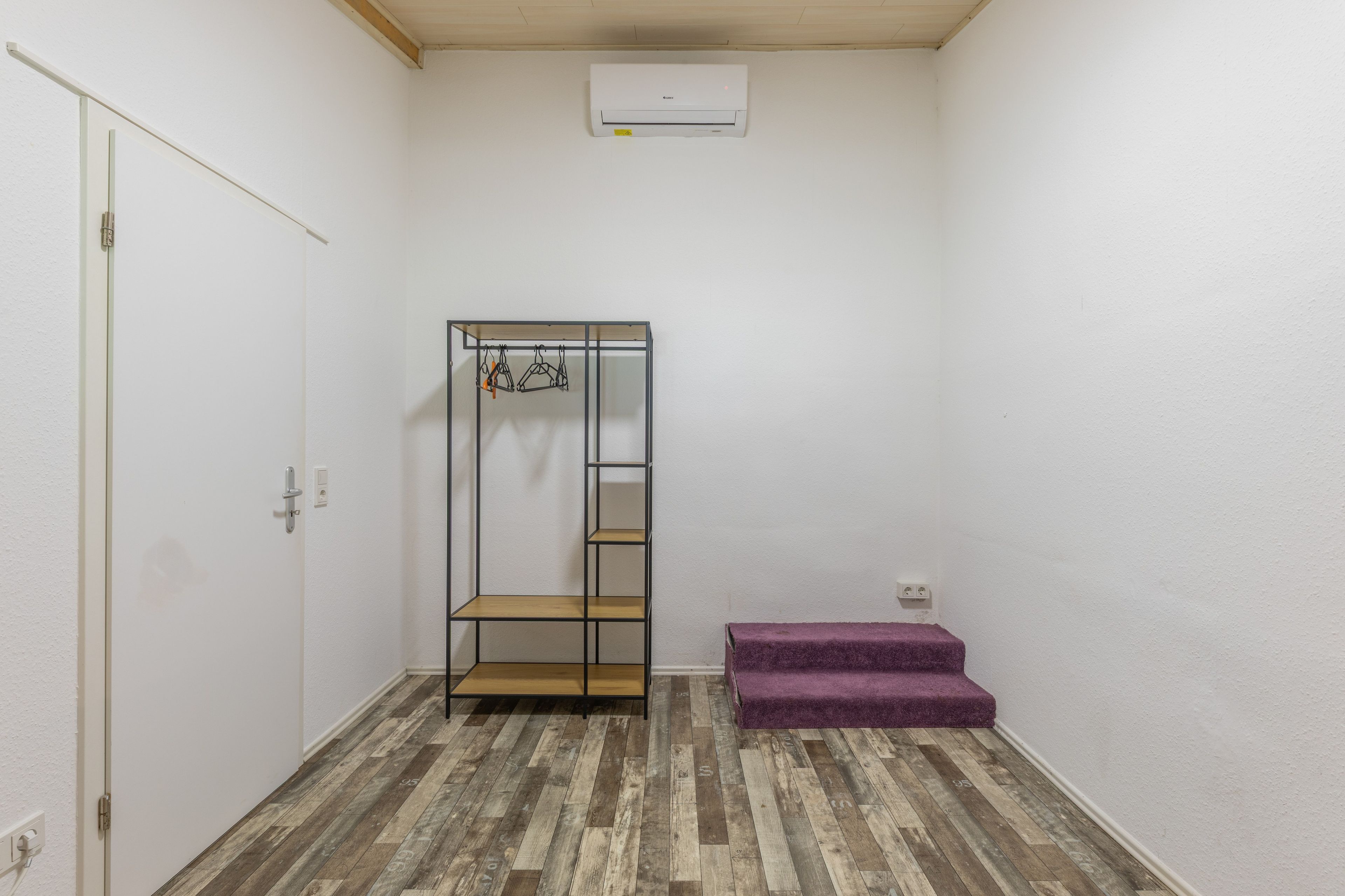 Quarto com guarda-roupa, um banco roxo e chão de madeira.