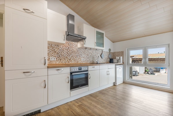 A modern kitchen with white cabinetry, a Bosch oven, and a view through a glass door to an outdoor area.
