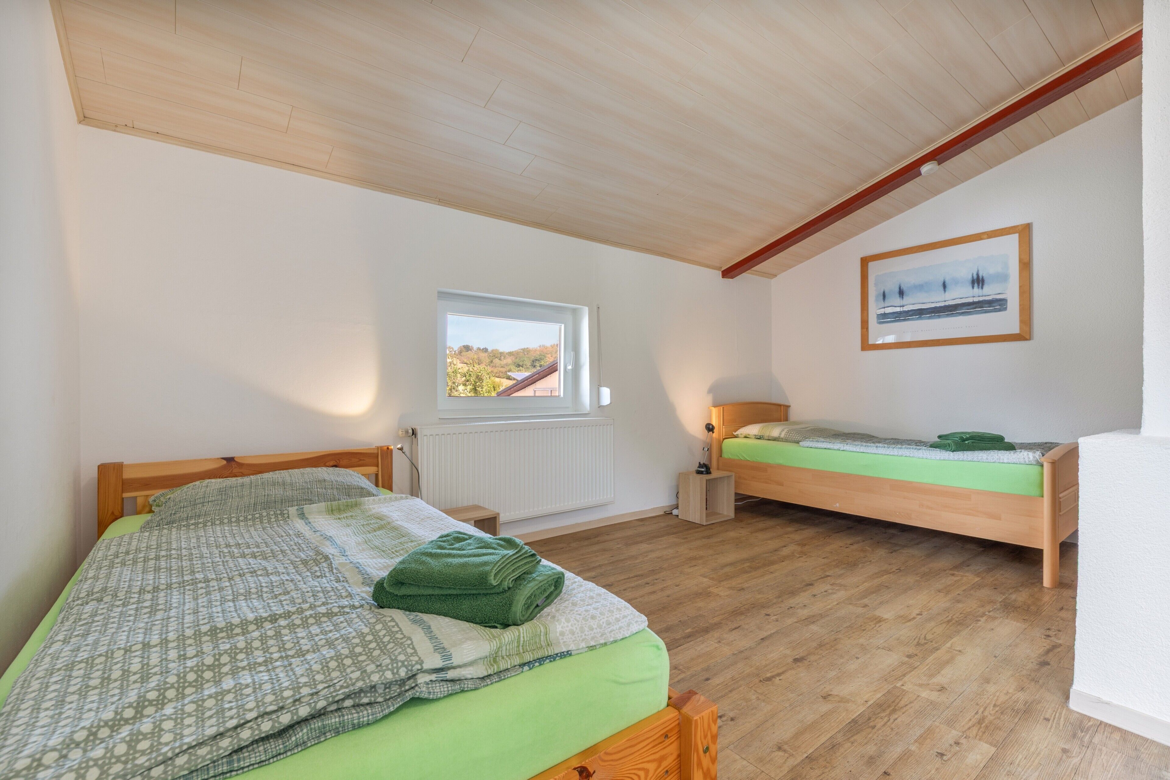 Quarto com duas camas de madeira, janela com vista, radiador e quadro pendurado na parede.